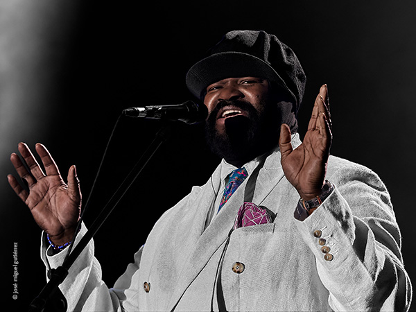 Retrato de Gregory Porter en plano medio cercano. Está cantando y mira sonriente a cámara con las manos abiertas.