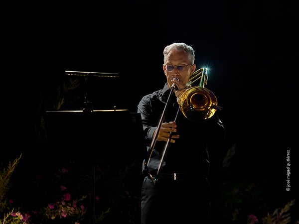 Retrato frontal en plano americano de Jan Smets tocando el trombón. Se ven abajo unas bonitas flores.